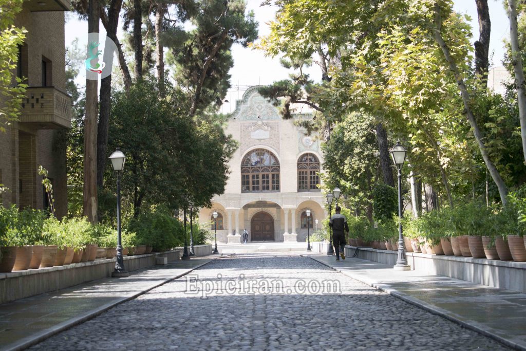 long sidewalk surrounded by trees that lead to masoudieh palace in tehran