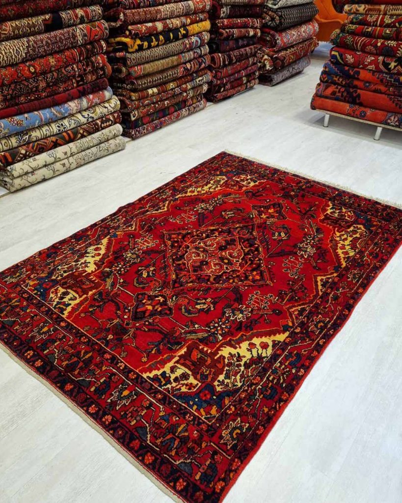 red persian rug spread on the floor next to many other rugs