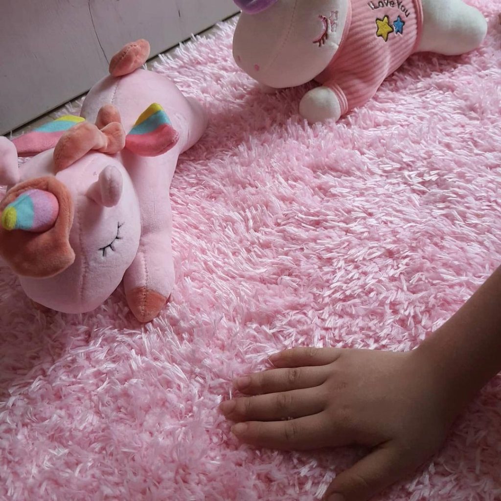 a baby's hand on the pink rug next to some pink unicorn dolls