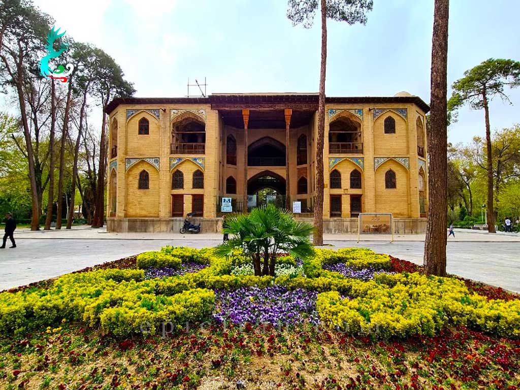 some yellow and purple flowers in a garden in front of the main monument of hasht behesht mansion in isfahan